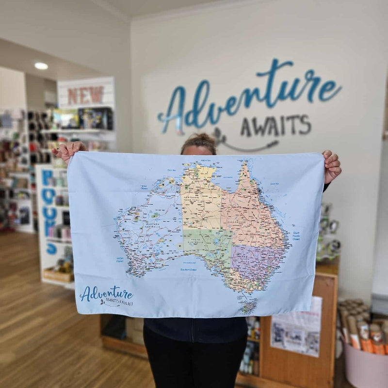 Person holding a map of Australia with 'Adventure Awaits' text in a store setting.