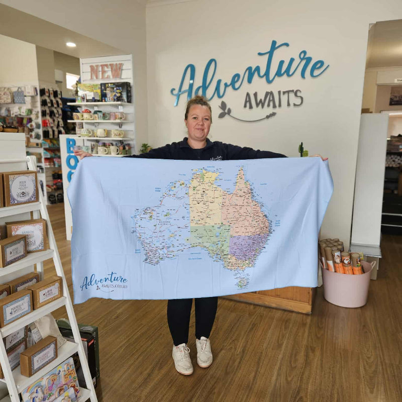 Person holding a large map of Australia in a store with 'Adventure Awaits' sign.