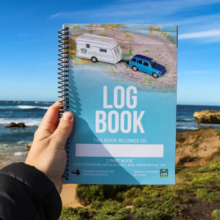 Hand holding a caravan log book with a scenic background of ocean and cliffs