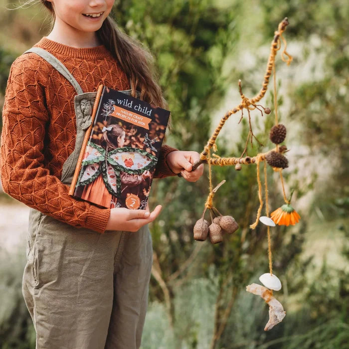 Child holding Wild Child nature craft book and handmade mobile outdoors — Adventure Awaits