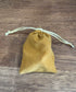Mustard drawstring pouch lying on a wooden tabletop for storing dice or game pieces — Adventure Awaits