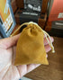Hand holding a mustard drawstring pouch for storing dice or small travel game pieces — Adventure Awaits