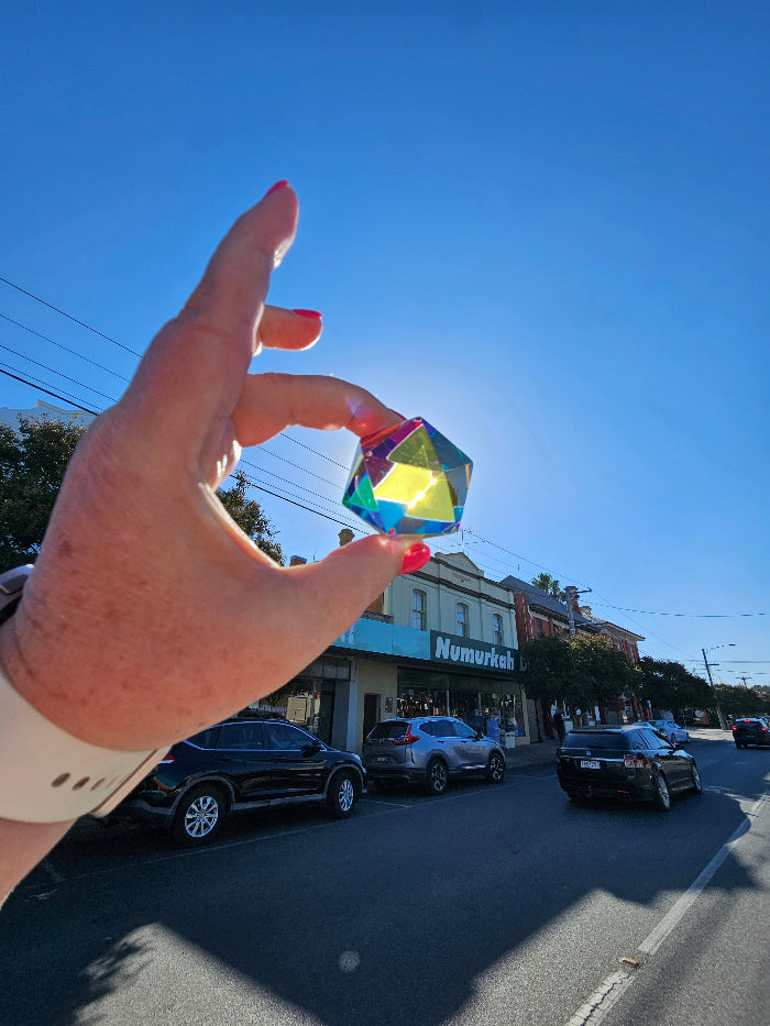 Hand holding Motus Mini CMY Cube in sunlight on Numurkah street, colourful travel fidget toy Adventure Awaits