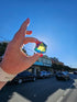 Hand holding Motus Mini CMY Cube in sunlight on Numurkah street, colourful travel fidget toy Adventure Awaits