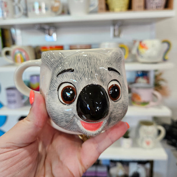 Person holding a cute koala-shaped mug with a blurred kitchen background