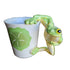Green frog-shaped handle on a white mug with a leaf design, set against a blurred background.