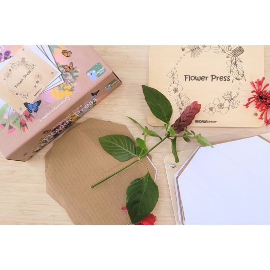 Australian Flora Flower Press kit beside fresh leaves, flowers and pressing paper on a wooden table, Adventure Awaits