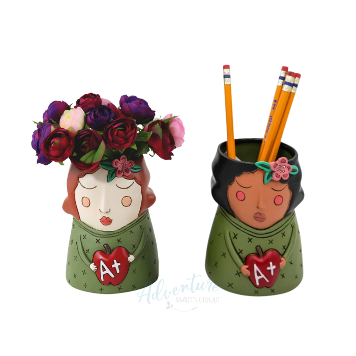 Two decorative pencil holders shaped like girls with flowers and apples, one holding pencils.