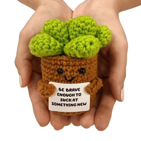 hands holding a handmade crochet broccoli plush toy with a funny motivational sign about trying something new