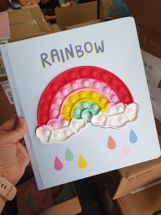 Hand holding Rainbow silicone pop it board book in store, colourful kids travel toy — Adventure Awaits