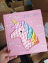 Hand holding Unicorn silicone pop it board book in store, pastel kids travel toy — Adventure Awaits