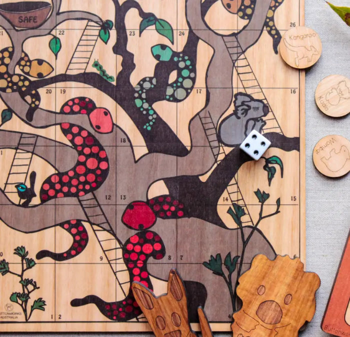 Close-up of Australian timber snakes and ladders board with native animal counters and wooden dice — Adventure Awaits