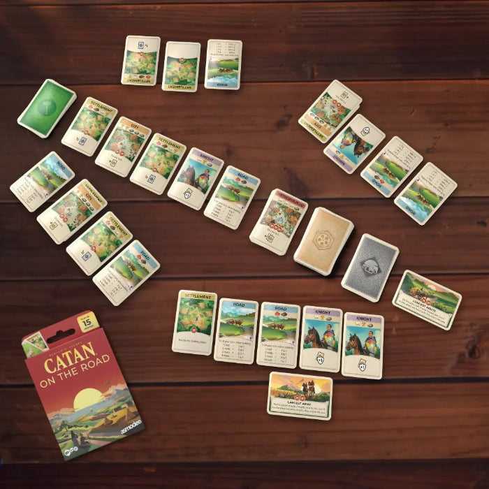CATAN On the Road card game laid out for play with colourful resource and development cards, Adventure Awaits