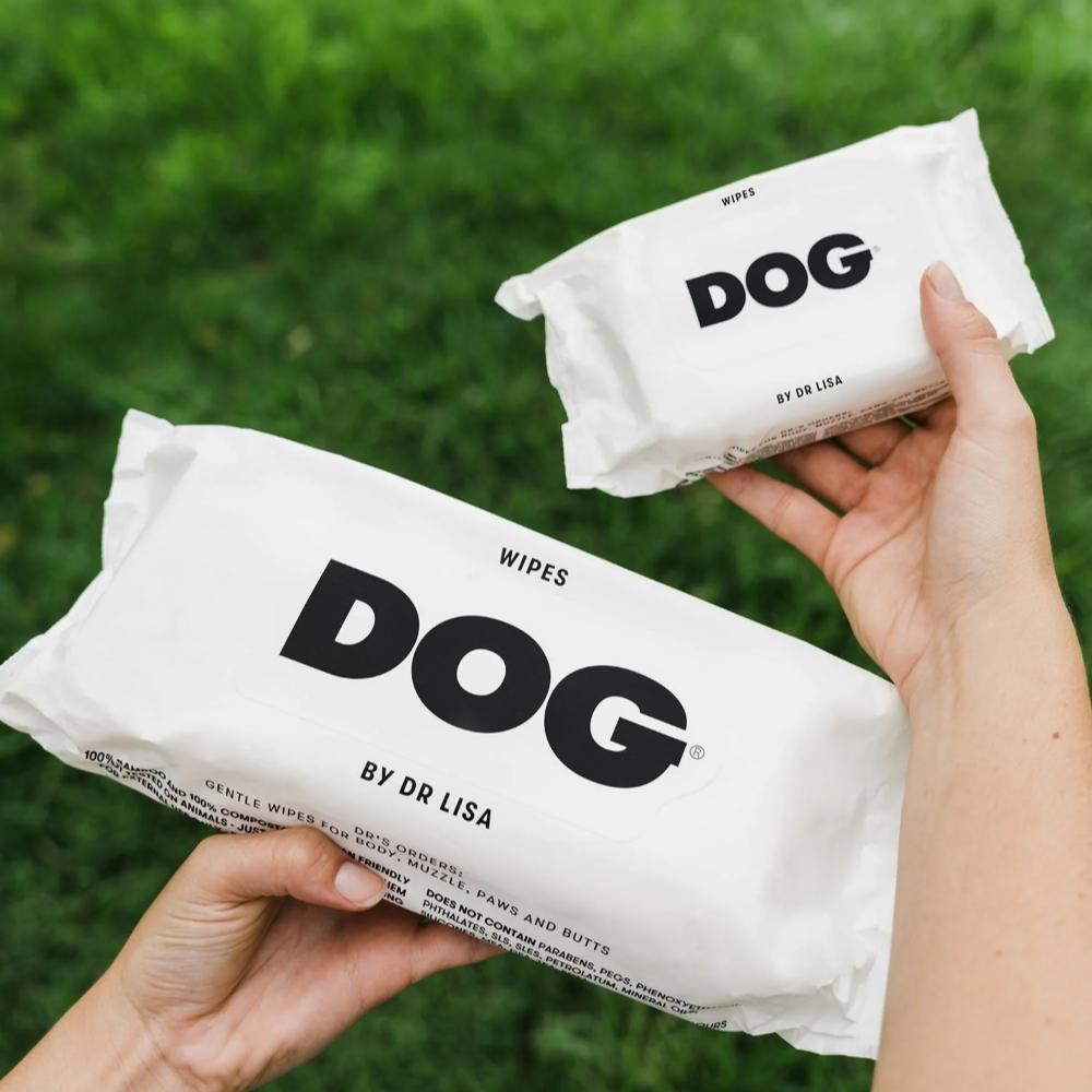 Two packages of 'DOG' wipes by Dr. Lisa held against a grassy background.