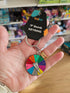 Hand holding a keyring with a colorful wheel and a black keychain labeled 'F Bomb Keyring' in a store setting.
