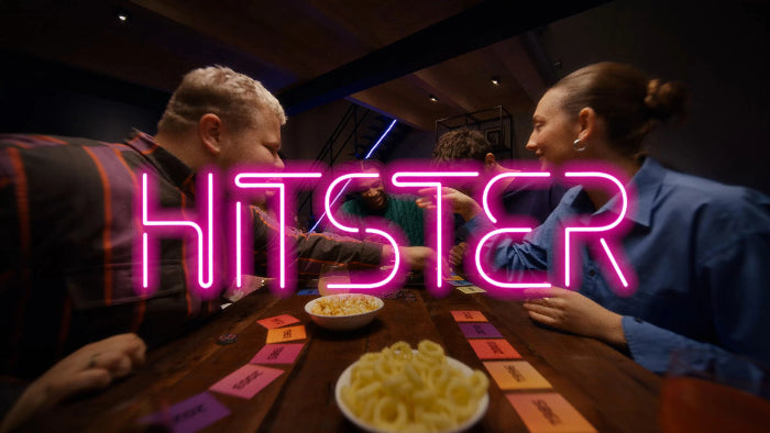 Friends lean across a table playing Hitster beneath a glowing neon logo — Adventure Awaits