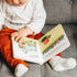 Child reading I Got You Some Kisses board book on grey couch — Adventure Awaits