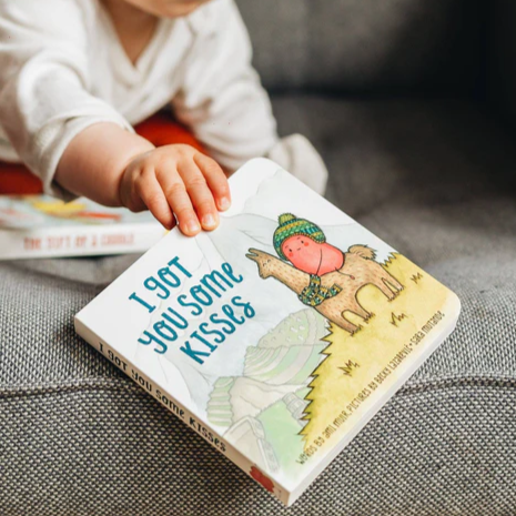 Child reaching for I Got You Some Kisses picture book on couch — Adventure Awaits