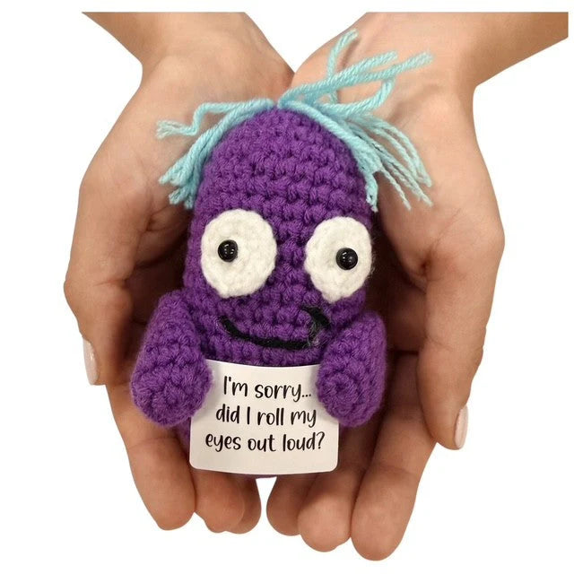 hands holding a quirky handmade crochet purple plush toy with a funny sarcastic quote sign