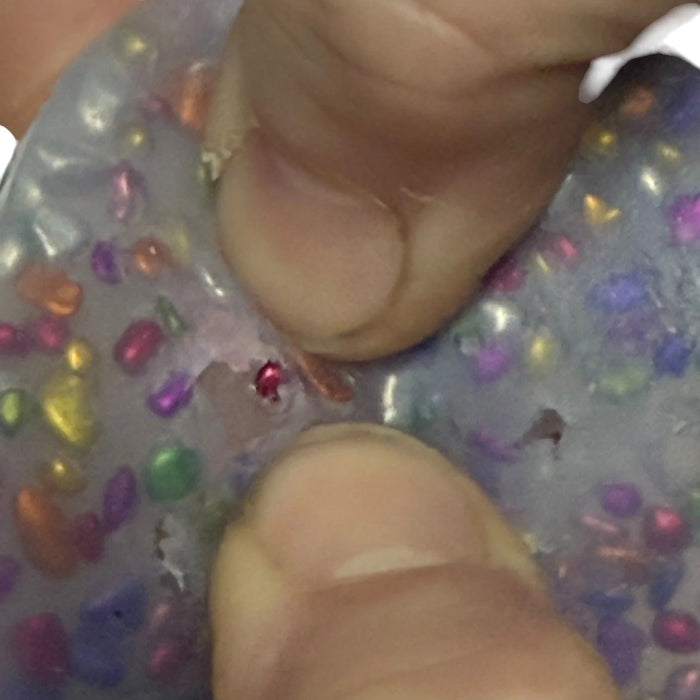 Close-up of hands interacting and picking gems out of a colourful gelatinous surface