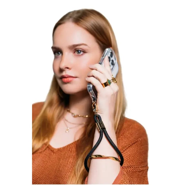 Woman holds a phone secured by a black wrist strap while taking a call, Adventure Awaits
