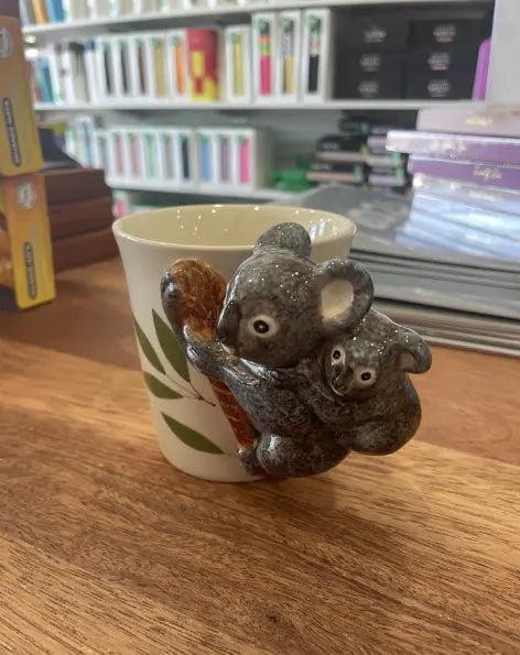 Cream koala mug with sculpted koala and joey handle beside eucalyptus leaves — Adventure Awaits