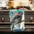 Kookaburra-themed kitchen towel hanging on a stove handle with a blurred kitchen background.