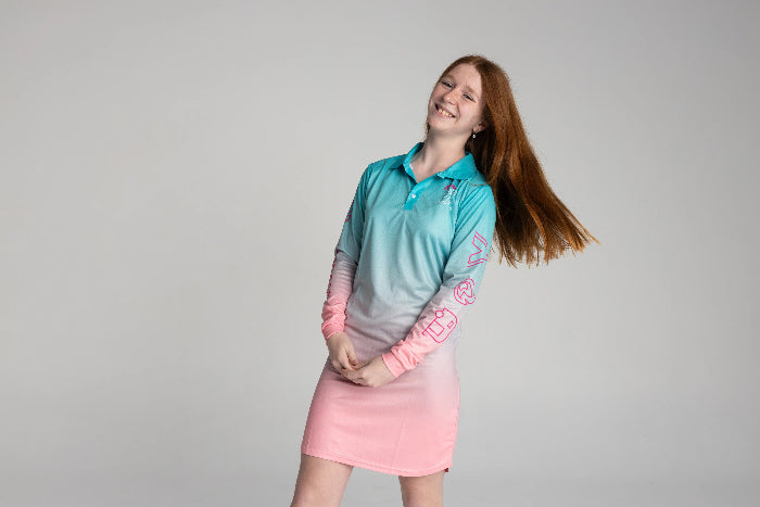 Girl smiling and tossing her hair in an aqua and pink long-sleeve UPF50+ fishing dress — Adventure Awaits