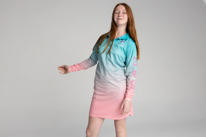 Girl posing in an aqua and pink long-sleeve UPF50+ fishing dress against a plain backdrop — Adventure Awaits