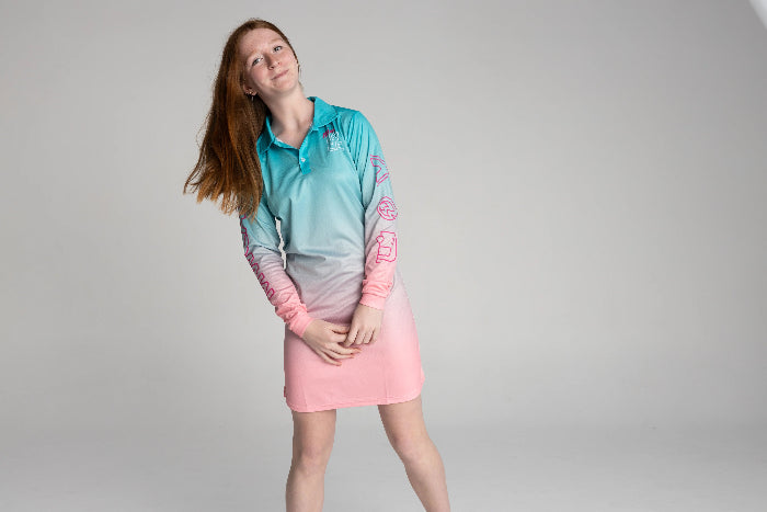 Girl smiling in an aqua and pink long-sleeve UPF50+ fishing dress against a plain backdrop — Adventure Awaits