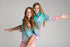 Two girls smiling in aqua and pink UPF50+ fishing dresses, one giving the other a piggyback — Adventure Awaits