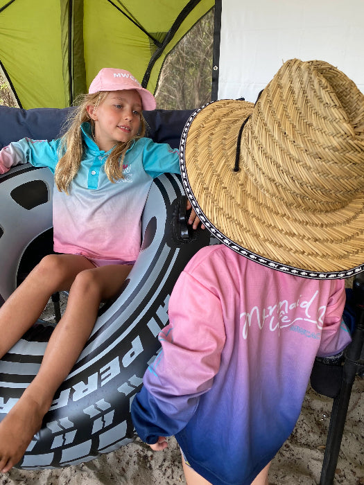 Two girls relaxing at a campsite in aqua, pink and navy long-sleeve fishing shirts and sun hats — Adventure Awaits