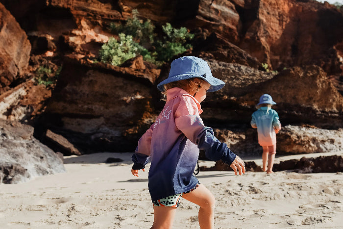 Kids exploring a rocky beach in pink, navy and aqua long-sleeve fishing shirts and sun hats — Adventure Awaits