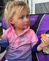 Girl eating a snack in a pink, purple and navy long-sleeve fishing shirt at a campsite — Adventure Awaits
