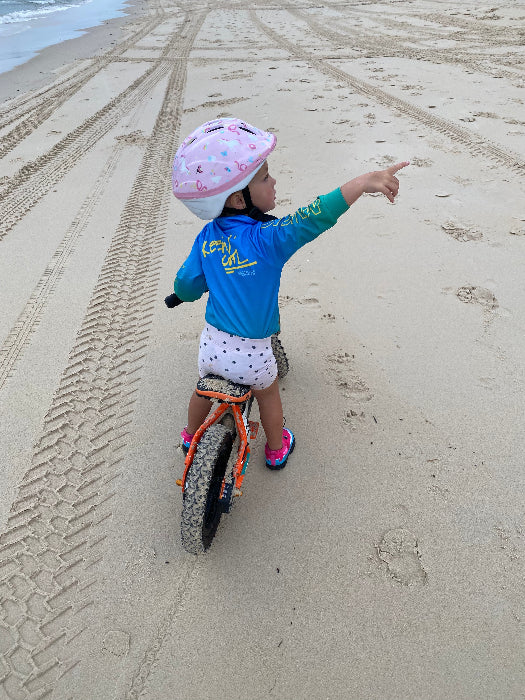 Child riding a balance bike on the beach in a blue and aqua long-sleeve fishing shirt — Adventure Awaits
