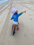 Child riding a balance bike on the beach in a blue and aqua long-sleeve fishing shirt — Adventure Awaits