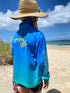 Back view of girl in a blue and aqua long-sleeve fishing shirt and straw hat walking by the beach — Adventure Awaits