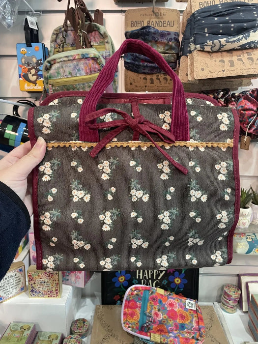 Floral roll up travel organiser bag with burgundy trim and tie closure displayed in store