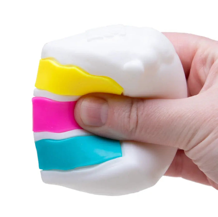 Hand squeezes a NeeDoh Piece O’ Cake sensory toy with white icing and colourful layered filling — Adventure Awaits