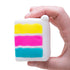 Hand holds a NeeDoh Piece O’ Cake squishy toy showing white icing with yellow, pink and blue layers — Adventure Awaits
