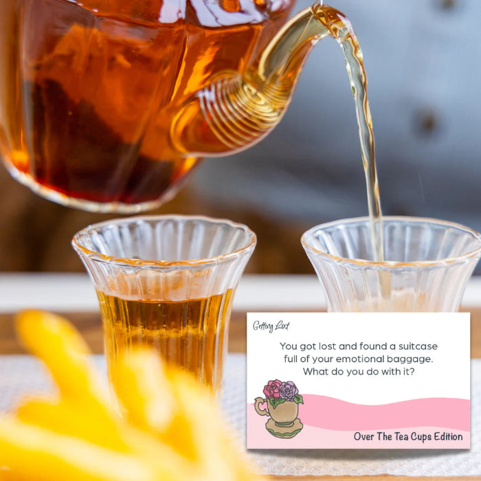 Tea pouring into glass beside Getting Lost Over The Tea Cups Edition conversation card — Adventure Awaits