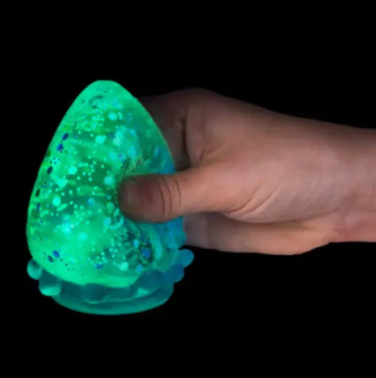 Hand squeezing green glow in the dark glitter drop squishy toy against black background — Adventure Awaits