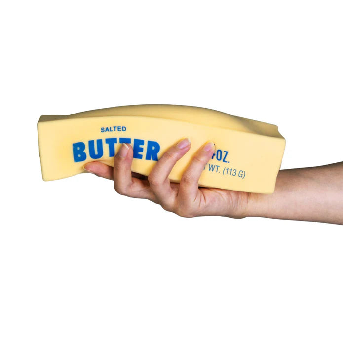 A hand holding a yellow novelty butter-shaped sponge with blue text reading 'SALTED BUTTER' on a plain white background.