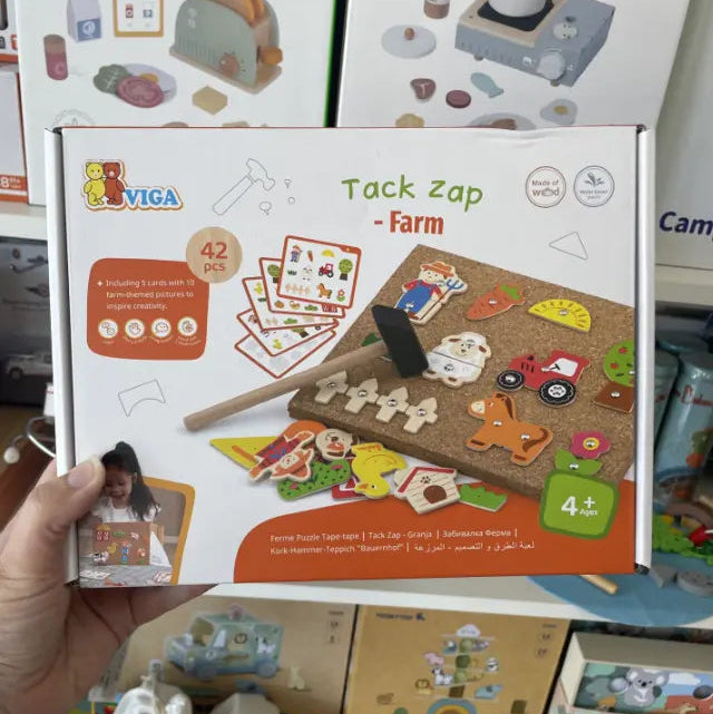 Hand holding VIGA Tack Zap Farm 42-piece box with cork board, wooden pieces and hammer — Adventure Awaits