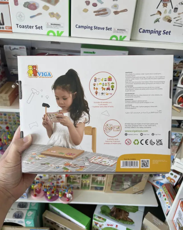 Hand holding back of VIGA Tack Zap Farm box with child using hammer and activity cards — Adventure Awaits