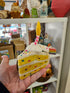 Hand holding a plush toy resembling a cake with colorful polka dots in front of a store shelf.