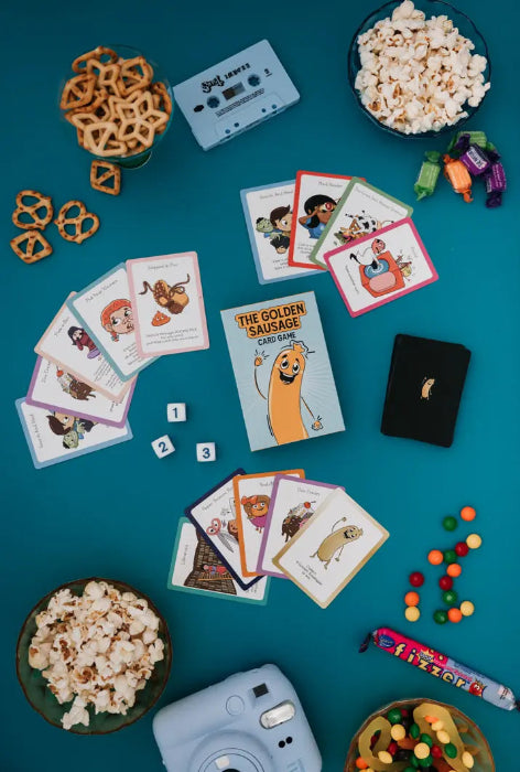 The Golden Sausage card game set out with cards, popcorn, pretzels and lollies — Adventure Awaits