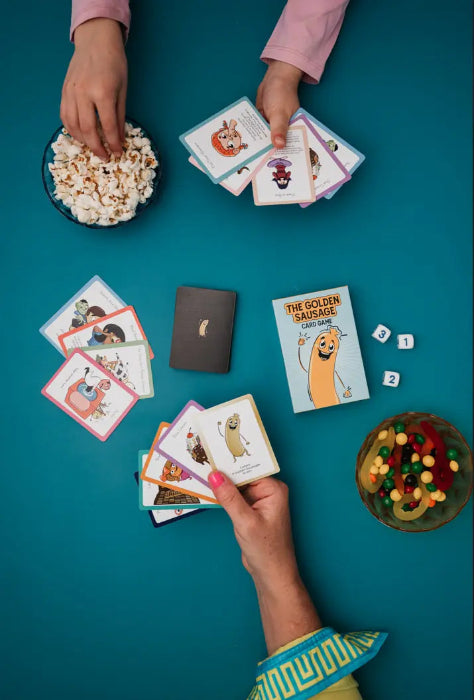 Two people playing The Golden Sausage card game with popcorn, lollies and number dice — Adventure Awaits