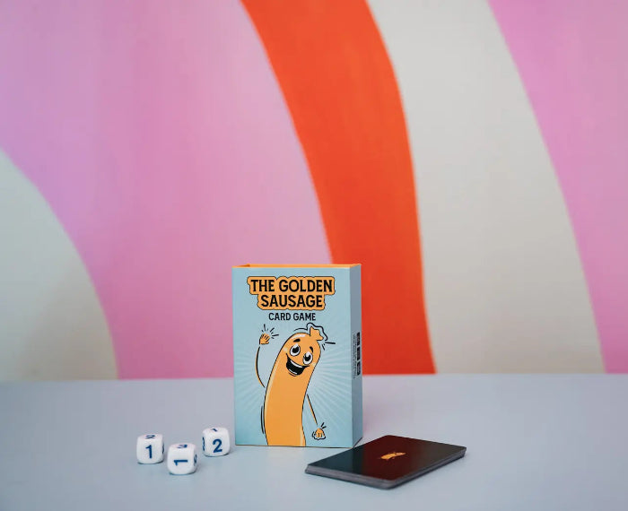 The Golden Sausage card game box with card deck and three number dice on colourful striped background — Adventure Awaits