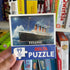 Hand holding Titanic 99 piece puzzle box in toy shop aisle — Adventure Awaits